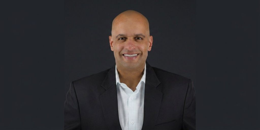 Portrait of Decision Point author Micah Maxwell wearing a dark blazer against a dark background.