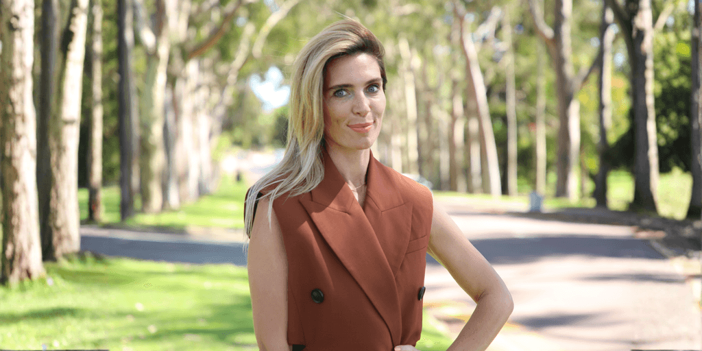 Aliya Pogorelskaya, Founder of Altinteg Technology Solutions, standing confidently outdoors in a sunlit park with a rust-brown blazer.