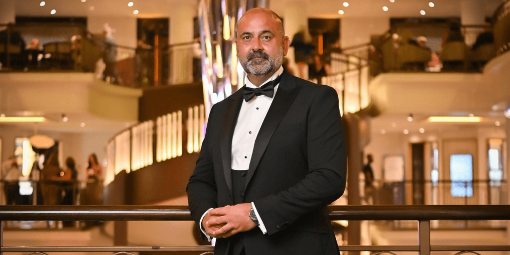 Man in black tuxedo posing confidently in an elegant hotel lobby.