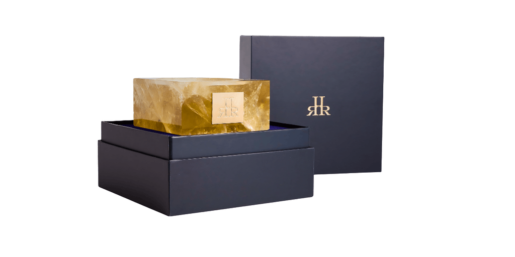 The image shows a luxurious home fragrance candle by RHR Luxury, encased in a gold crystal vessel, symbolizing artisanal craftsmanship and premium design.