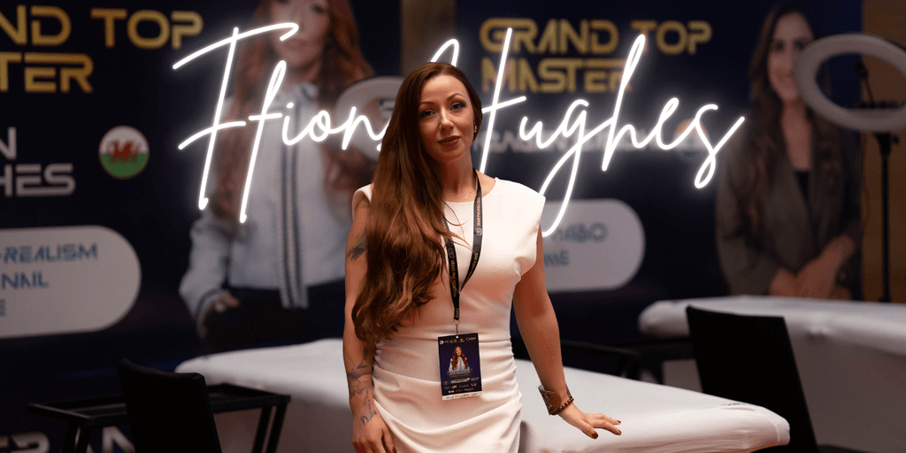 Ffion Hughes, a CEO and entrepreneur, standing confidently at an event. She is wearing a white dress and has long hair. With a badge around her neck, she poses in front of a promotional banner with her name, "Ffion Hughes," illuminated in neon lights. The background suggests a professional event related to entrepreneurship and beauty, reflecting her leadership in empowering women in business.