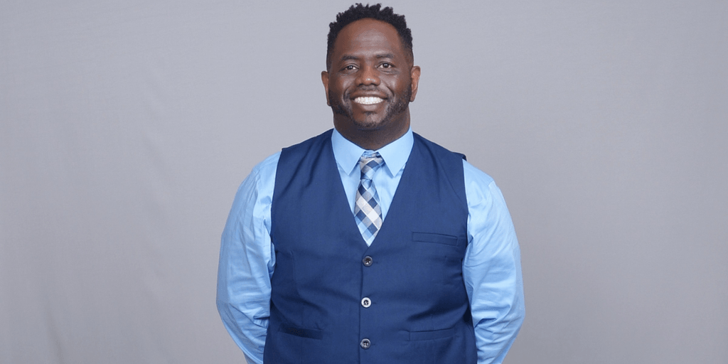 Rashad Woods smiling in a blue vest and tie, founder of The T.R.O.N. Podcast promoting meaningful global conversations.