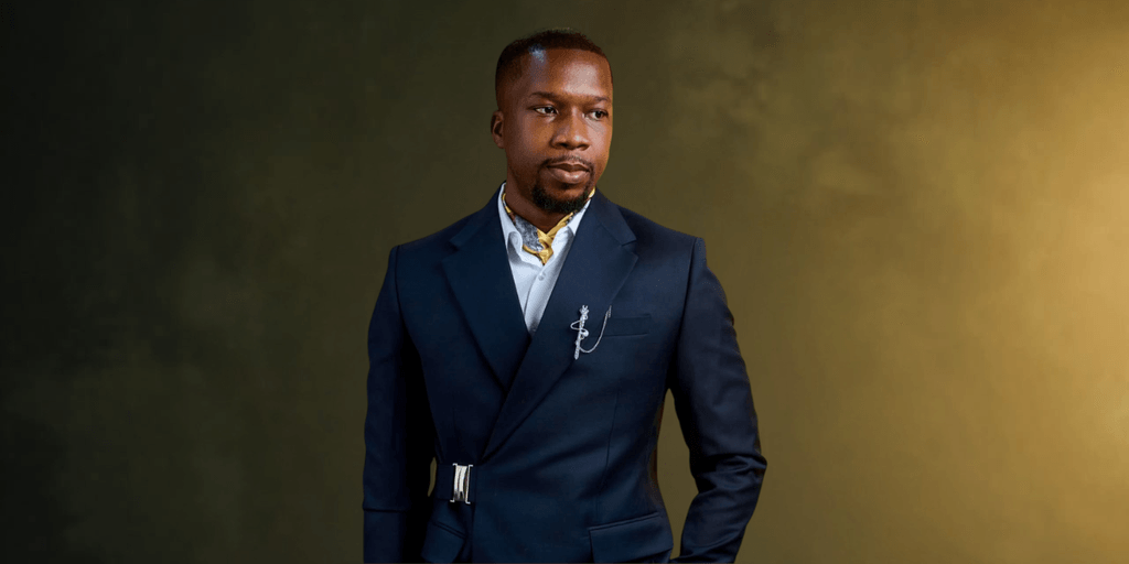 A man in a stylish navy suit stands confidently against a textured background