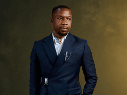 A man in a stylish navy suit stands confidently against a textured background
