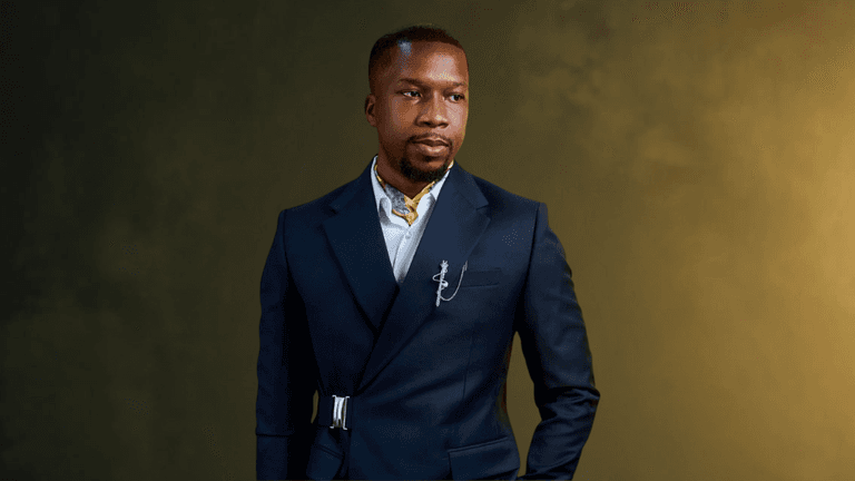 A man in a stylish navy suit stands confidently against a textured background