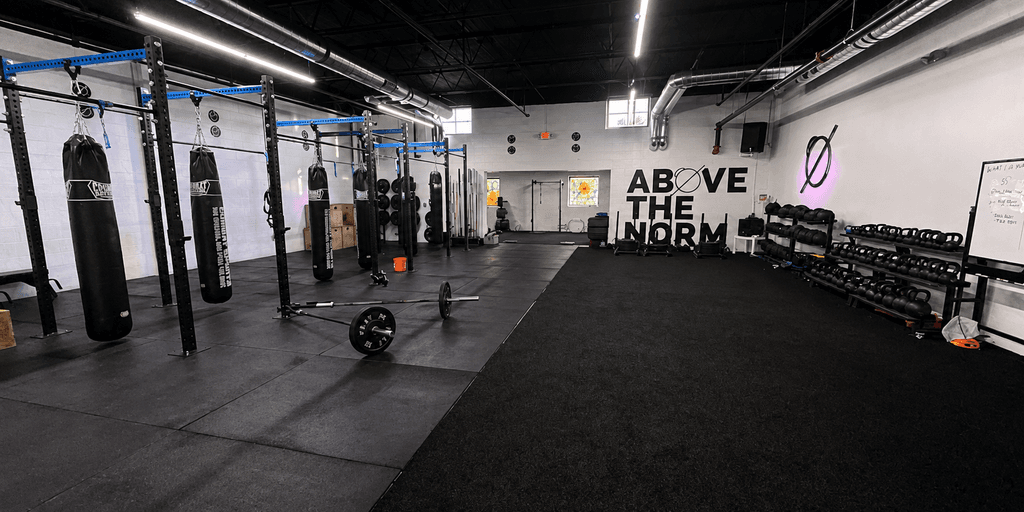 Interior of a gym featuring punching bags, kettlebells, and workout space on black flooring