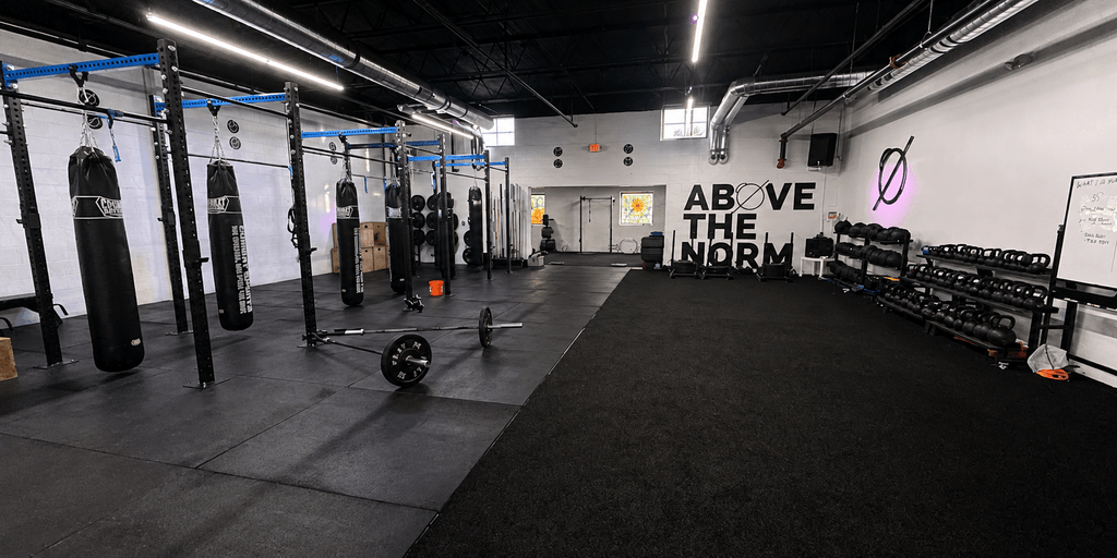 Interior of a gym featuring punching bags, kettlebells, and workout space on black flooring
