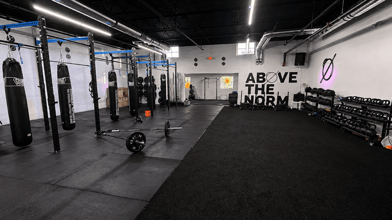 Interior of a gym featuring punching bags, kettlebells, and workout space on black flooring