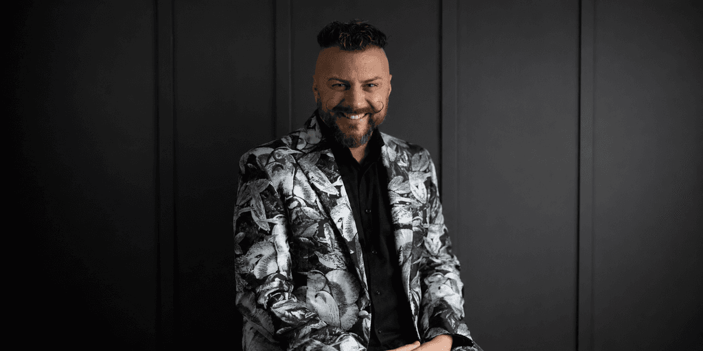 Man wearing a patterned blazer smiles against a dark background
