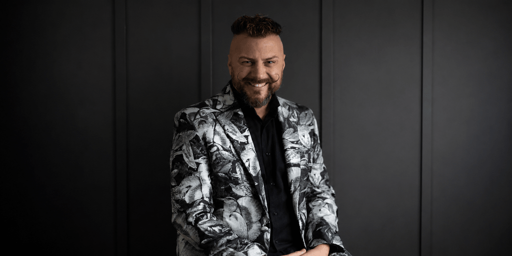 Man wearing a patterned blazer smiles against a dark background