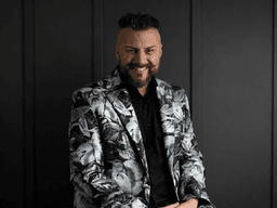 Man wearing a patterned blazer smiles against a dark background