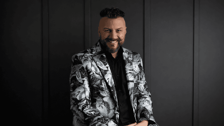 Man wearing a patterned blazer smiles against a dark background
