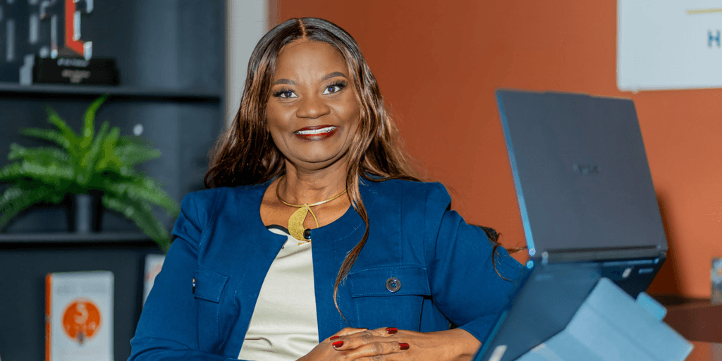 Professional woman smiling confidently at a desk with a laptop and plants in background