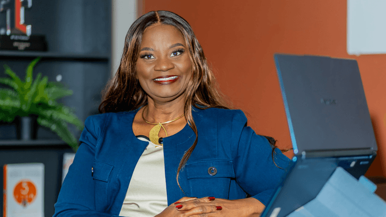 Professional woman smiling confidently at a desk with a laptop and plants in background