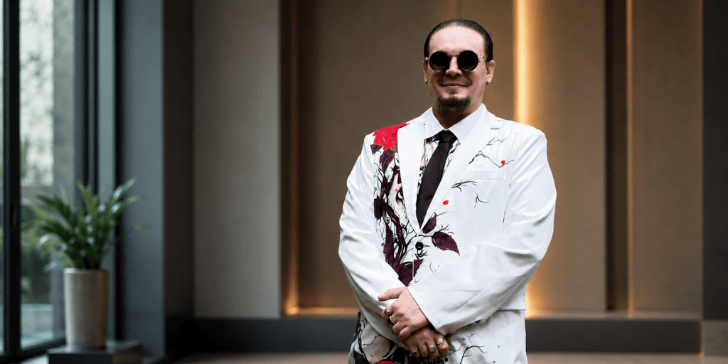 A man in a stylish floral suit and sunglasses stands confidently indoors