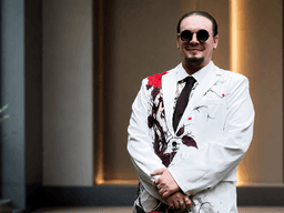 A man in a stylish floral suit and sunglasses stands confidently indoors