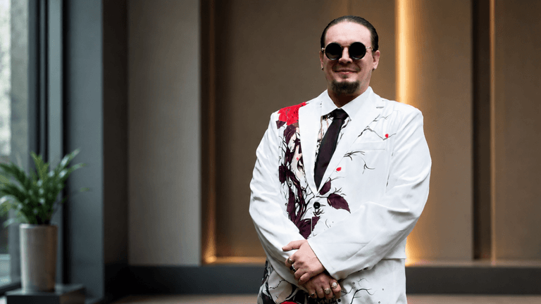 A man in a stylish floral suit and sunglasses stands confidently indoors