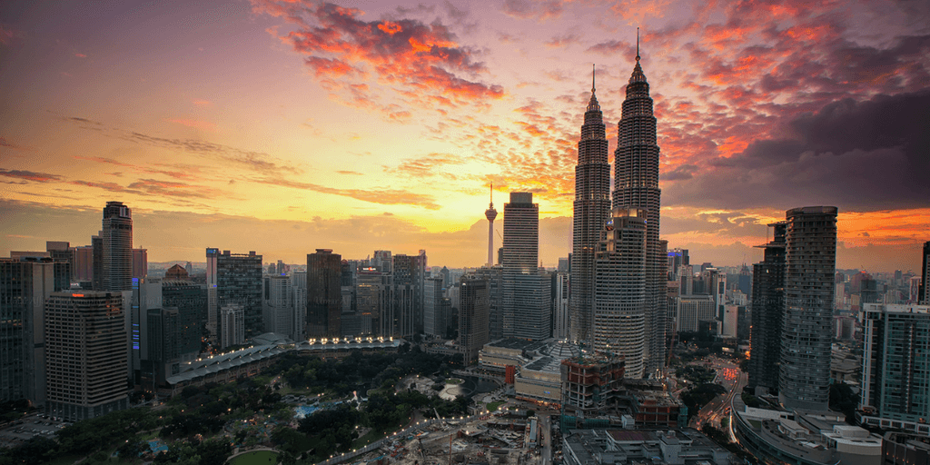 City skyline at sunset featuring Petronas Towers and vibrant cloud colors.