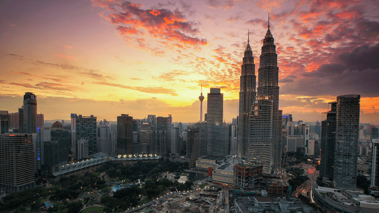 City skyline at sunset featuring Petronas Towers and vibrant cloud colors.