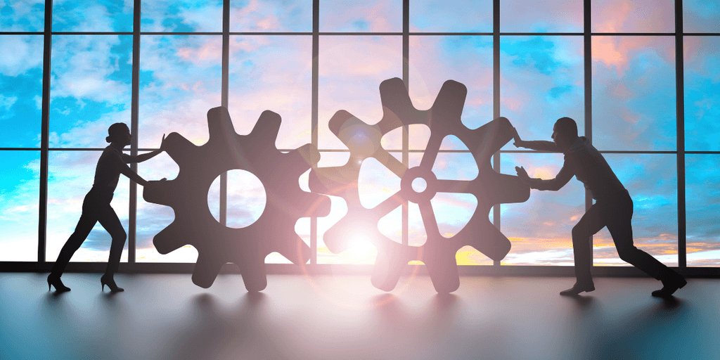 Silhouettes of a man and a woman pushing large gears against a sunset backdrop