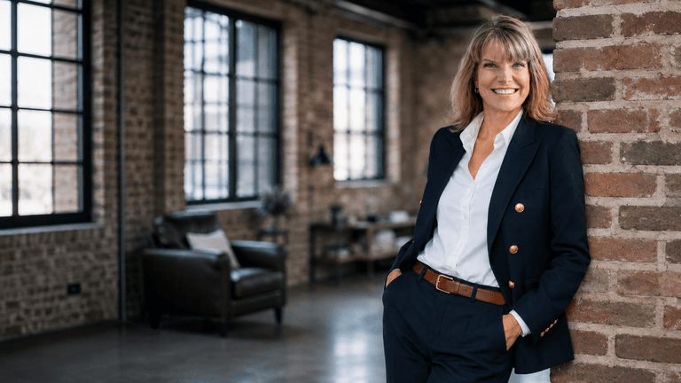Confident woman in a blazer standing against a brick wall in a modern interior