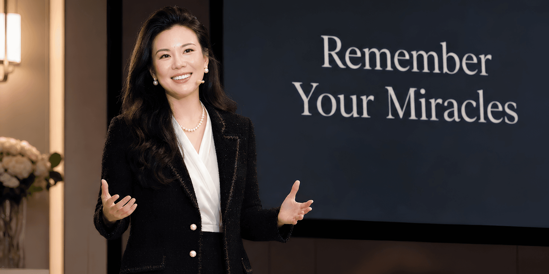 A woman in a black blazer speaks confidently in front of a presentation screen