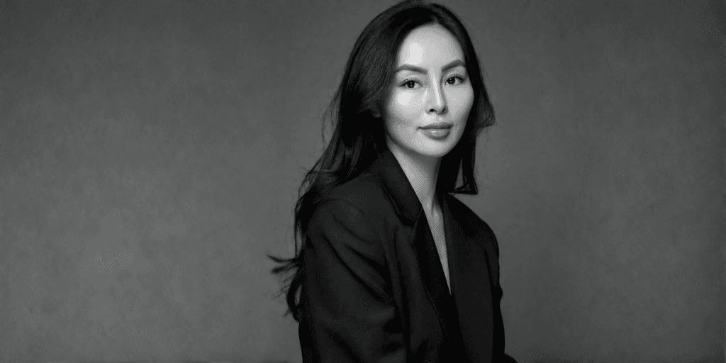 A woman in a black suit poses against a neutral gray background
