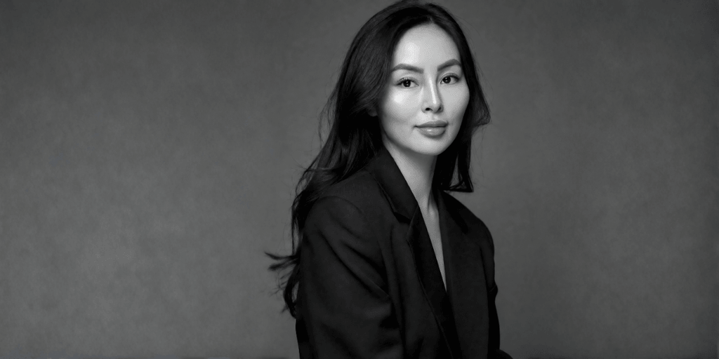A woman in a black suit poses against a neutral gray background