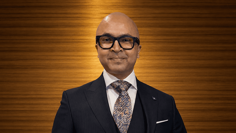 Man in a suit and glasses smiling against a wooden background