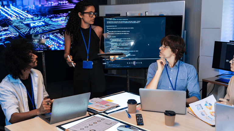 A diverse group collaborating in a tech meeting with digital presentations and coding on screens