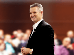 A man in a suit smiles confidently in front of an audience.
