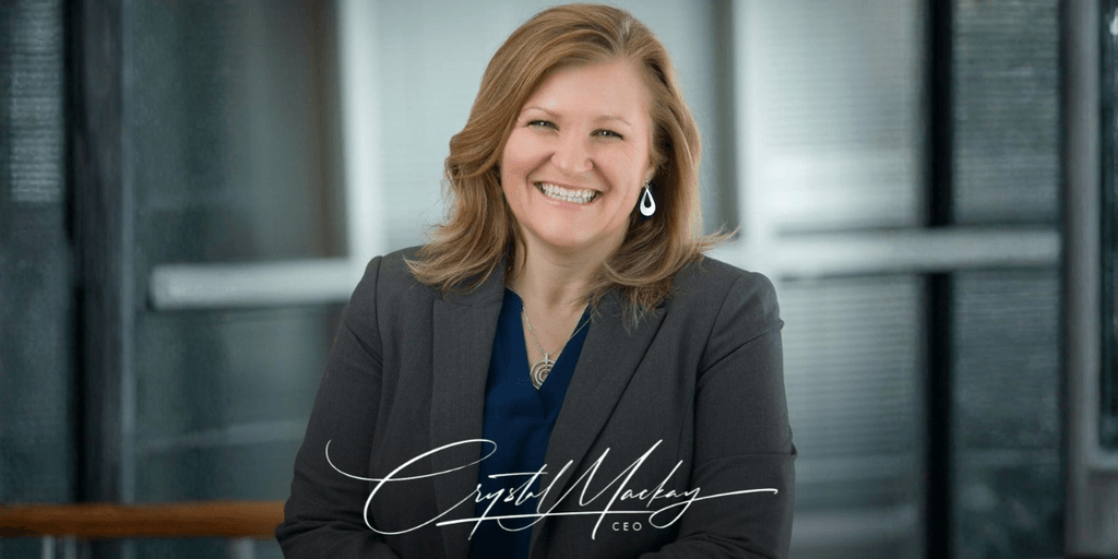 Smiling woman in a blazer poses in an office setting with a professional demeanor