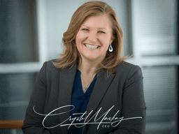 Smiling woman in a blazer poses in an office setting with a professional demeanor