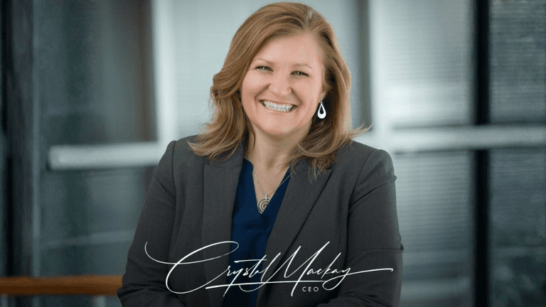 Smiling woman in a blazer poses in an office setting with a professional demeanor