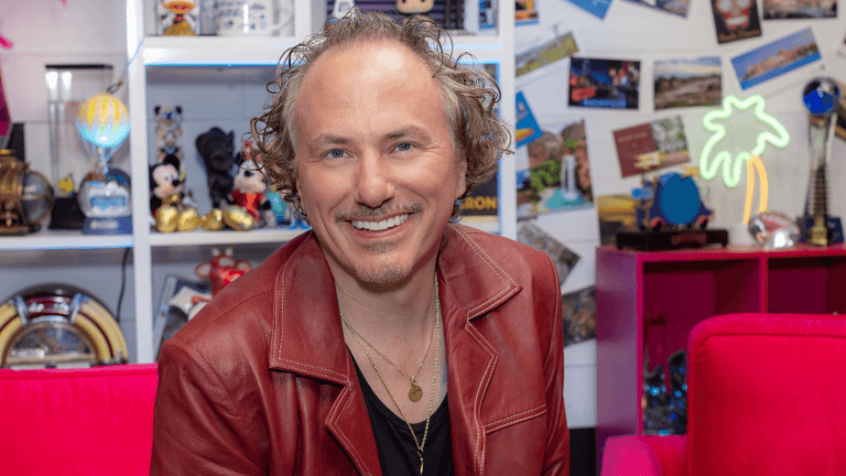 A smiling man in a red jacket poses against a colorful, playful background