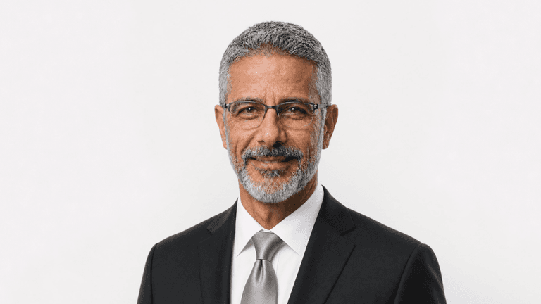 Man with gray hair and beard in a suit and glasses against a white background