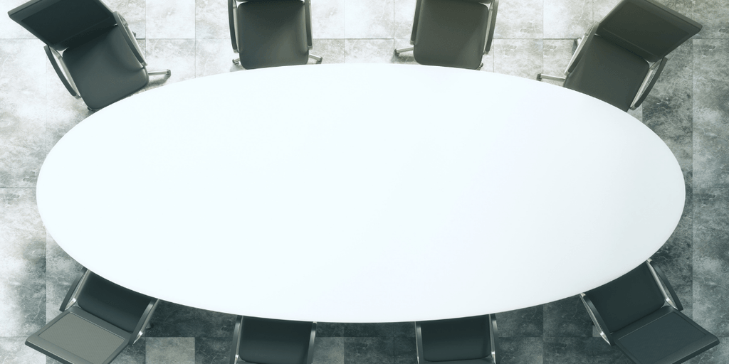 Aerial view of an oval conference table surrounded by black chairs.