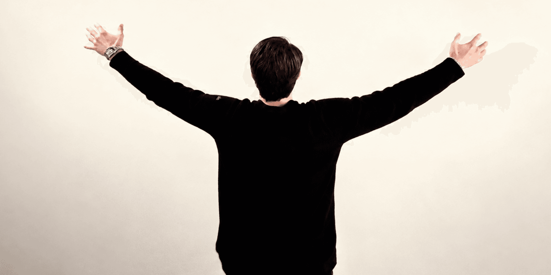 A person stands with arms outstretched, facing away against a neutral background.