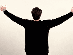 A person stands with arms outstretched, facing away against a neutral background.