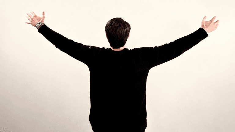 A person stands with arms outstretched, facing away against a neutral background.