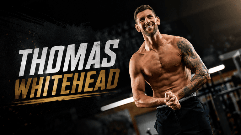 Fit man with tattoos smiling in a gym setting, showcasing strength and positivity