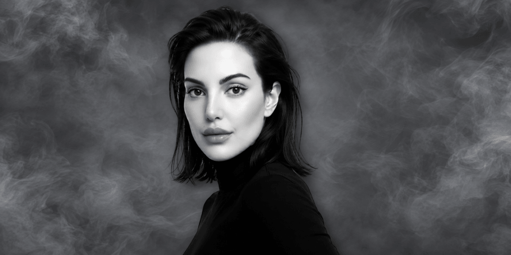 A woman with long dark hair poses against a smoky black background