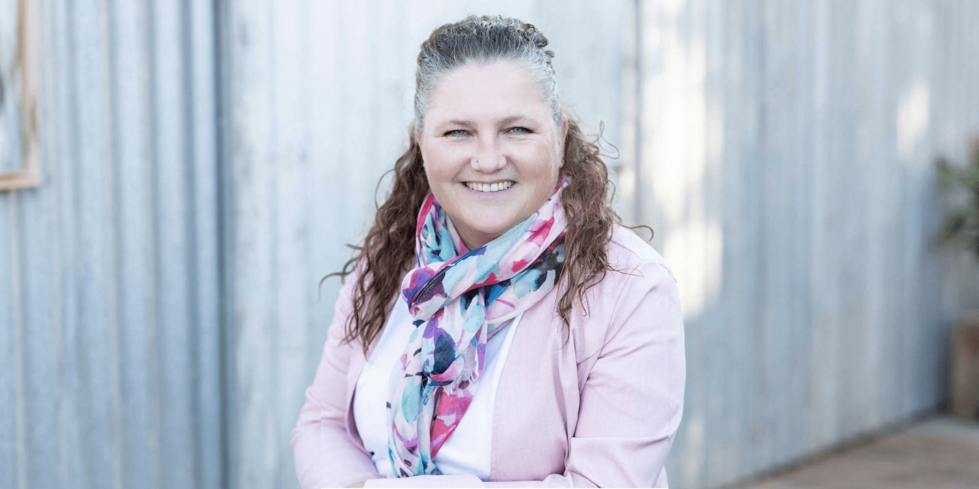 Smiling woman with curly hair wearing a colorful scarf and light jacket outdoors