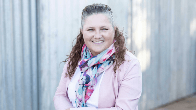 Smiling woman with curly hair wearing a colorful scarf and light jacket outdoors