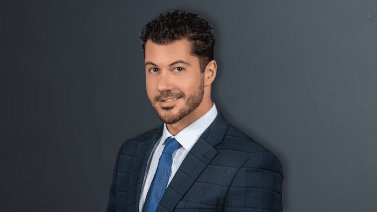 Man in a suit and tie with a stylish hairstyle against a dark background