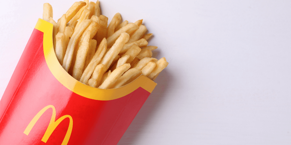 Heap of golden French fries in a red McDonald's container on a white surface