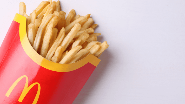 Heap of golden French fries in a red McDonald's container on a white surface