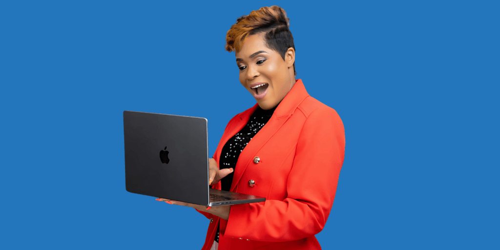 Woman in a red blazer holding a laptop, smiling against a blue background