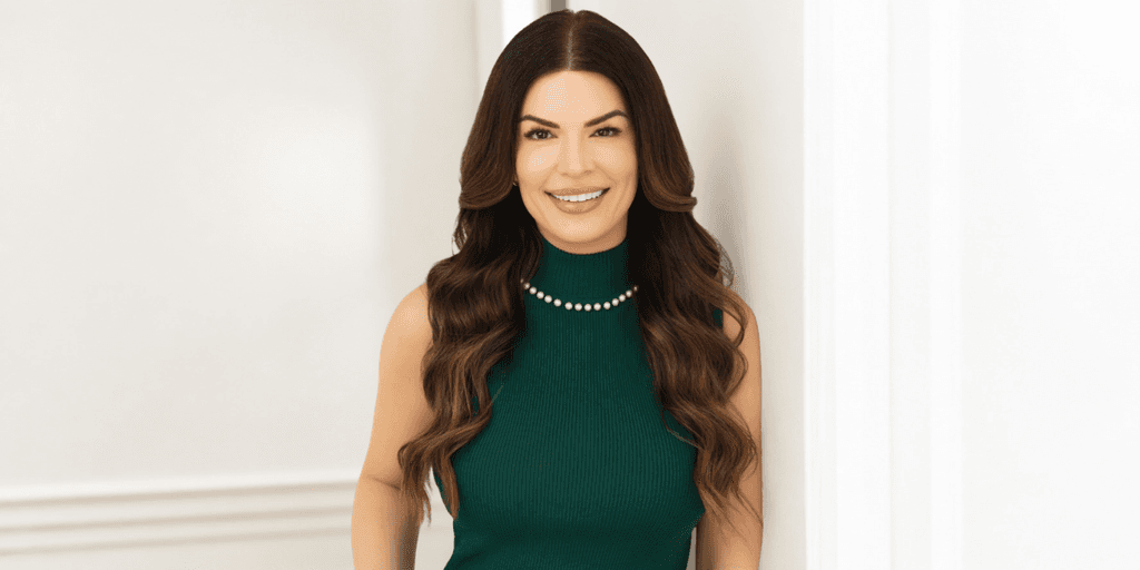 Smiling woman in a green dress with long, wavy hair standing by a wall