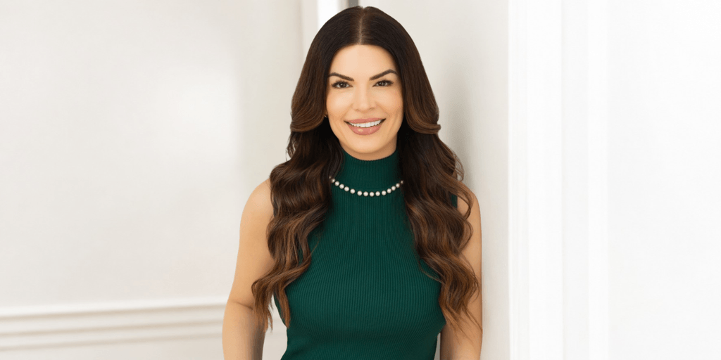 Smiling woman in a green dress with long, wavy hair standing by a wall
